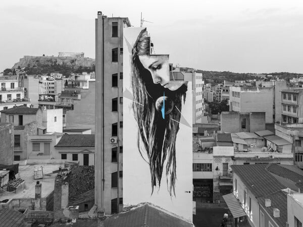 Ο ΙΝΟ ζωγραφίζει στα κτίρια της Αθήνας κρεμασμένος με σχοινιά