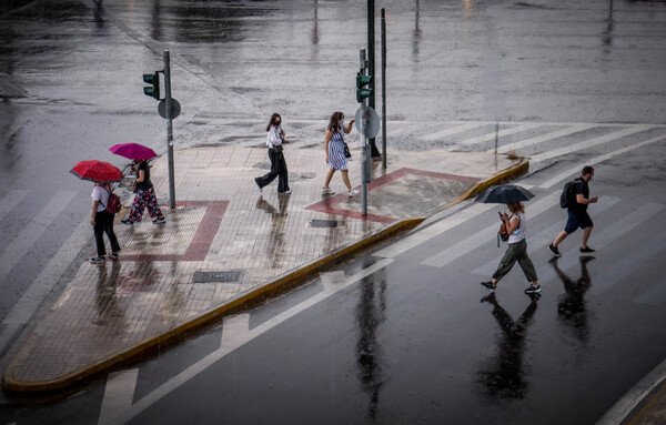 Κόσμος περπατά μέσα στη βροχή με ομπρέλες